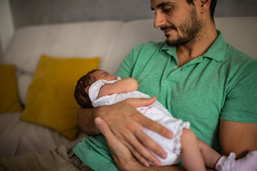 Male in green shirt seated while holding infant