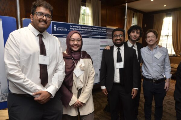 A group of students stand in front of the planetary scorecard poster smiling.
